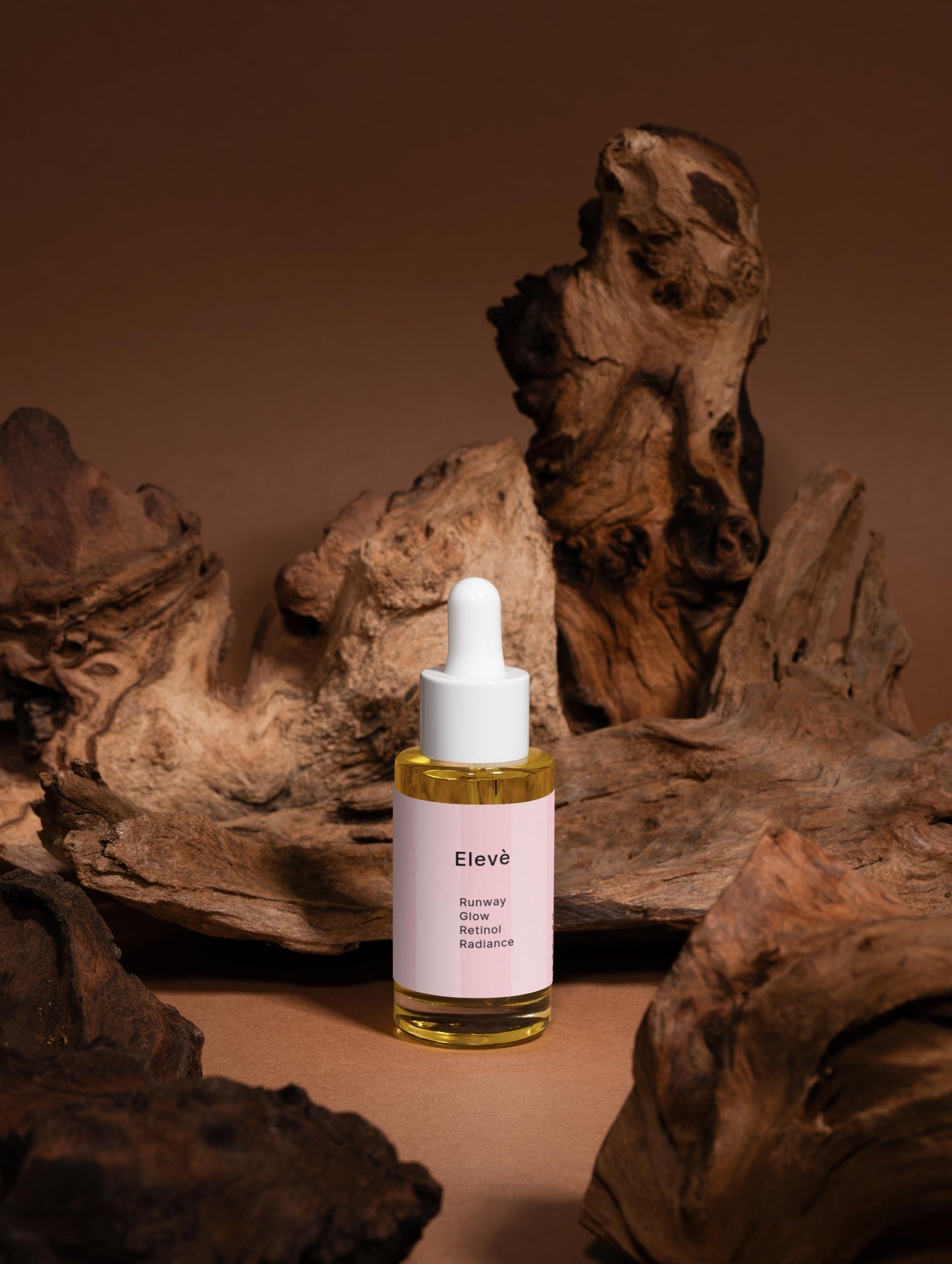 Elevè Runway Glow Retinol Alternative Oil Serum-Vorderseite des Flakons vor braunem Hintergrund mit Holzelementen.Luxuriöses Anti-Aging-Ölserum mit Bakuchiol und nährenden Bio-Ölen für glattere, strahlende und revitalisierte Haut. 