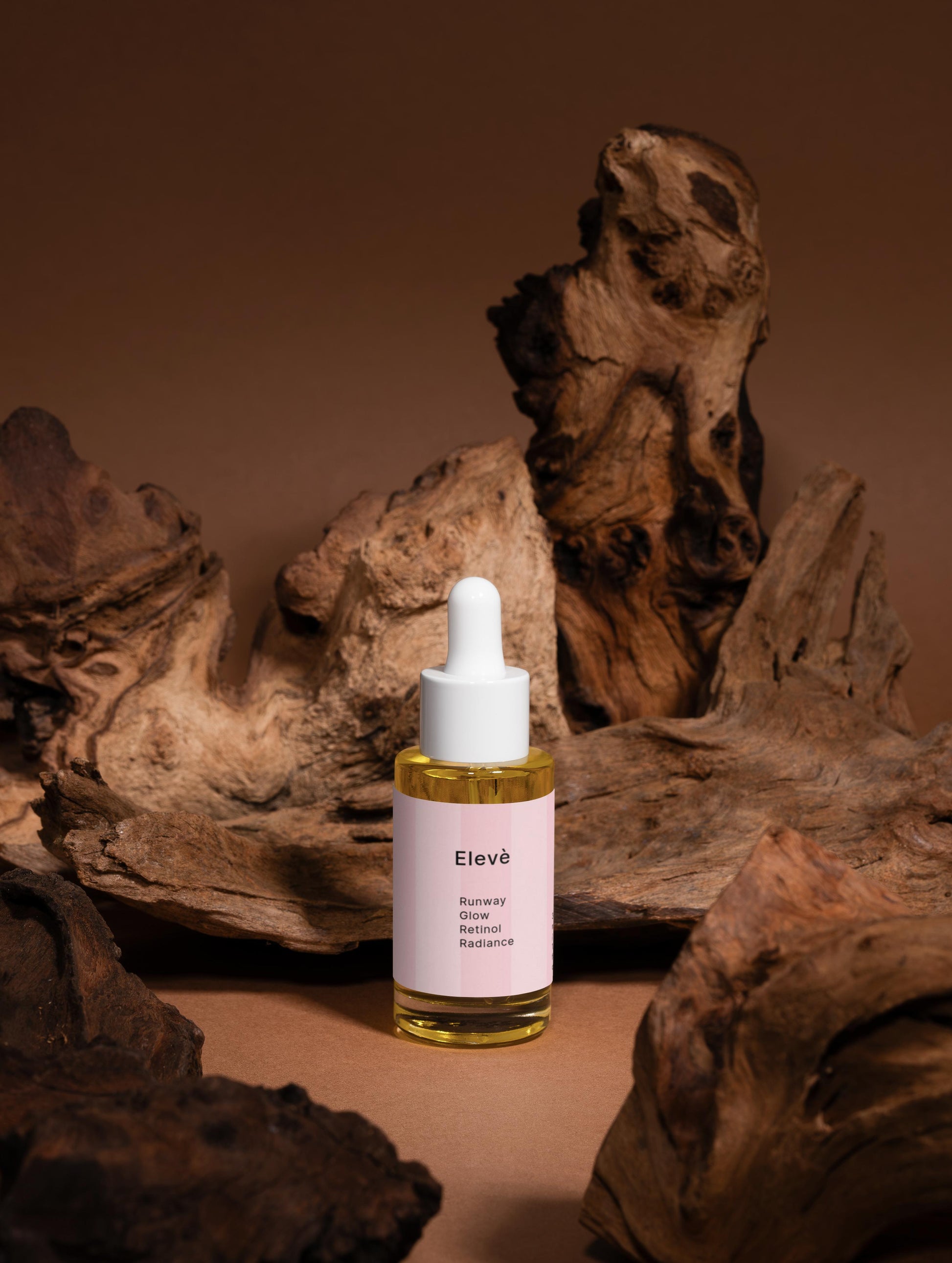 Elevè Runway Glow Retinol Alternative Oil Serum-Vorderseite des Flakons vor braunem Hintergrund mit Holzelementen.Luxuriöses Anti-Aging-Ölserum mit Bakuchiol und nährenden Bio-Ölen für glattere, strahlende und revitalisierte Haut. 