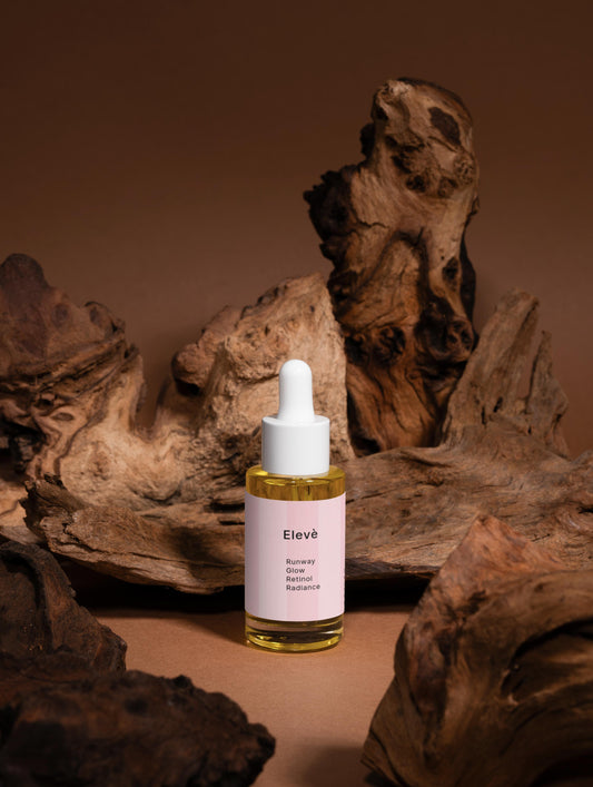 Elevè Runway Glow Retinol Alternative Oil Serum-Vorderseite des Flakons vor braunem Hintergrund mit Holzelementen.Luxuriöses Anti-Aging-Ölserum mit Bakuchiol und nährenden Bio-Ölen für glattere, strahlende und revitalisierte Haut. 
