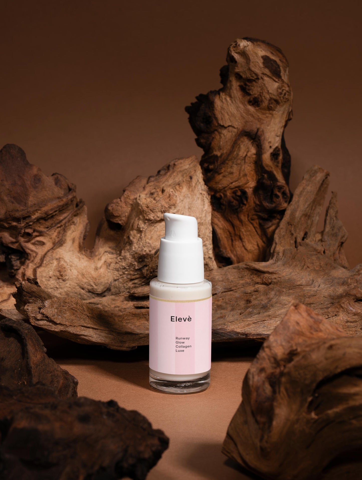 Elevè Hydrating Glow Serum  vor braunem Hintergrund mit natürlicher, holziger Deko.Luxuriöses, feuchtigkeitsspendendes Anti-Aging-Serum in transparanter,weißer Luxusflasche- mit Hyaluronsäure und Sodium PCA für glatte, pralle und strahlende Haut. 